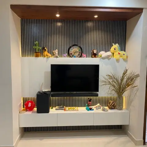 Family TV alcove with charcoal fluted panelling behind a white floating console, a backlit display ledge lined with soft toys and a wall clock