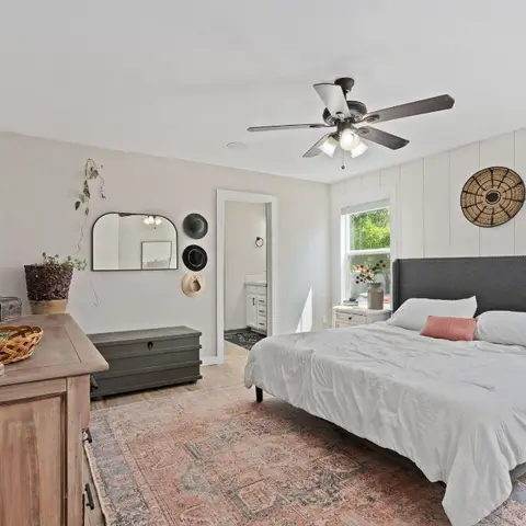 Farmhouse-style bedroom with a grey nailhead-trim bed, shiplap accent wall, wooden dresser styled with candlesticks, and a layered vintage-pattern rug.