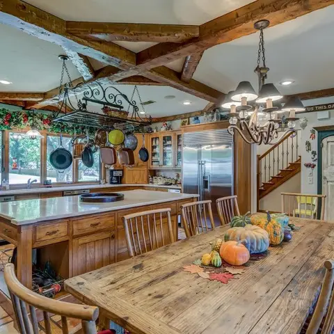 Farmhouse-style dining table set with autumn gourds beneath a wrought-iron chandelier