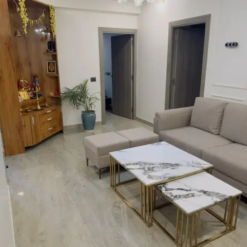 Flat living room with a beige L-sofa and two gold-framed marble-top nesting tables in the foreground