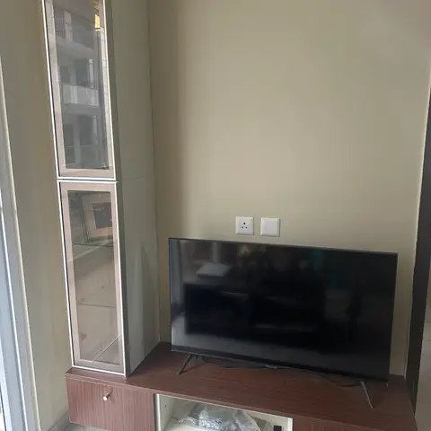 Floating walnut-laminate TV console paired with a tall glass-front display cabinet against a plain wall.