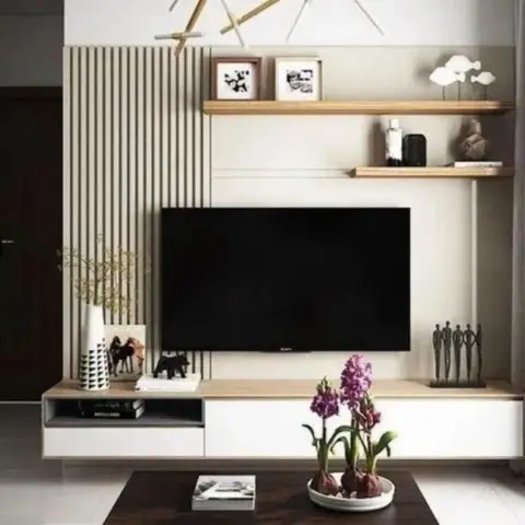 Floating white-and-wood TV console beneath a fluted vertical wall panel, with styled floating shelves and a gold branch chandelier.