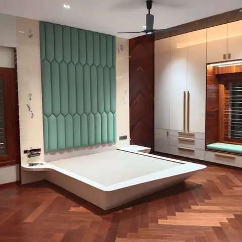 Floating white platform bed against a scalloped teal upholstered headboard wall with a herringbone wood floor and gold-handled wardrobe.