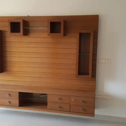 Floating wood-panelled TV unit with display niches on either side and a bank of drawers below, mounted on a bare wall in an otherwise empty room.