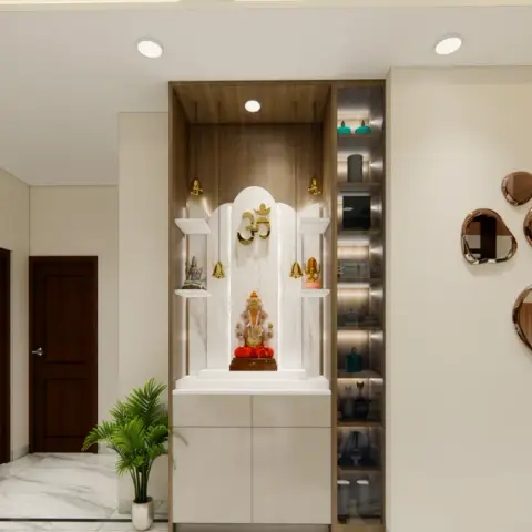Floor-standing white pooja unit with an arched marble backdrop, gold Om and hanging brass bells, set in a wood-lined recess beside a slim backlit curio column