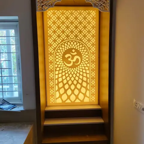 Floor-to-ceiling built-in mandir in a window corner, its backlit CNC jaali panel carrying an Om inside an arch
