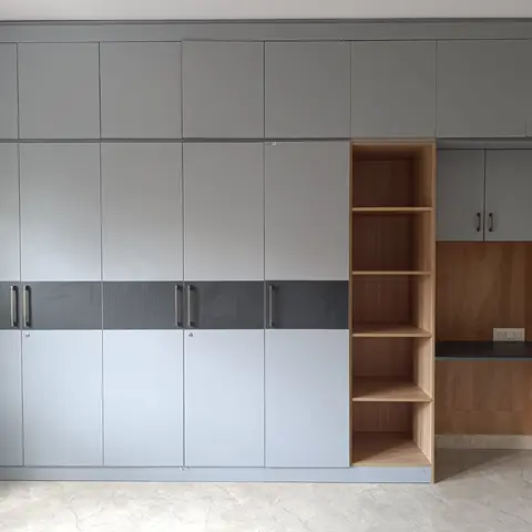 Floor-to-ceiling two-tone grey wardrobe wall transitioning into an open-shelf study nook with a floating wood-laminate desk.