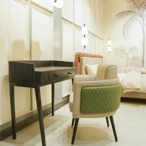 Fluted black writing desk with a stone top under a three-globe wall light, a green-and-cream quilted armchair pulled up to it