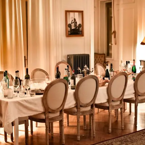 Formal dining room set for a dinner party with a long white-clothed table, ten oval-back wood dining chairs, warm lamp lighting