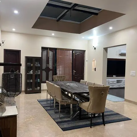 Formal dining room with a dark marble-top table and eight upholstered chairs on a striped rug, a wood-and-glass display cabinet
