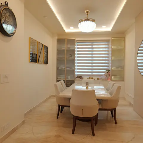 Formal dining room with a marble-top table and cream upholstered chairs, fluted-glass crockery cabinets flanking a zebra-blind window