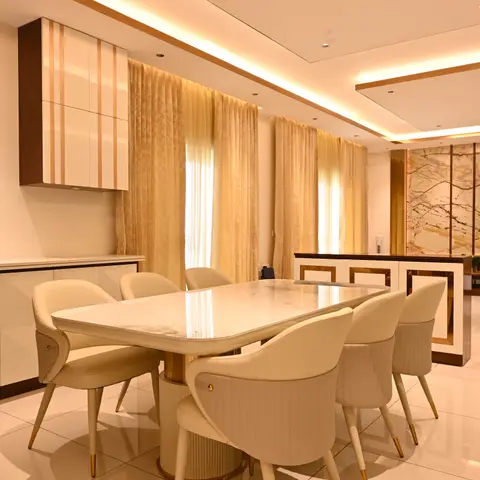 Formal dining room with a marble-top table, brass-trimmed cream leather chairs and a gold-edged cove-lit ceiling against a marble feature wall