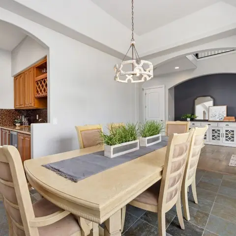 Formal dining room with a wood pedestal table set for six under a drum-shaped pendant chandelier, dark slate tile floor