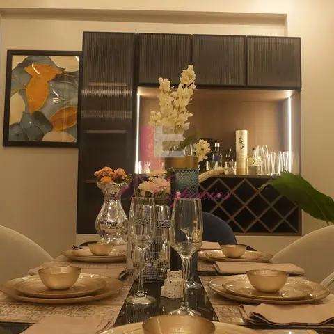 Formal dining table set with gold-rimmed plates and crystal glassware, backed by a fluted dark-wood bar and crockery unit with a diamond-lattice wine rack