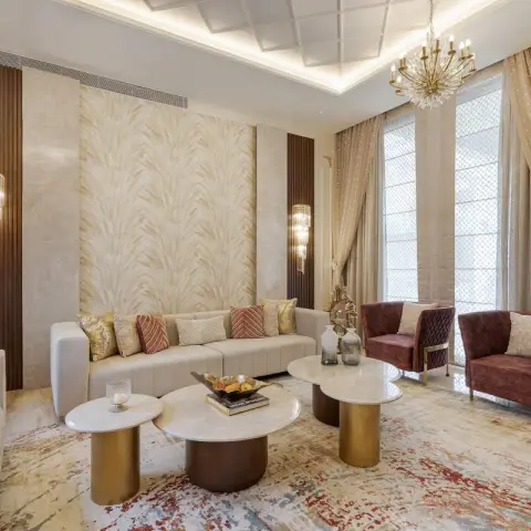 Formal double-height sitting room with ivory channel-tufted sofas, maroon quilted velvet armchairs on brass legs, a cluster of round marble-and-brass tables