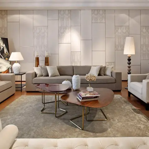 Formal drawing room lined with cream embossed deco panelling, three grey sofas around kidney-shaped walnut and oxblood tables on a faded grey rug
