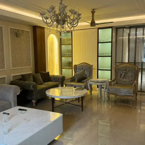 Formal drawing room with a crystal chandelier over an olive tufted chesterfield, carved gilt wing chairs on polished marble