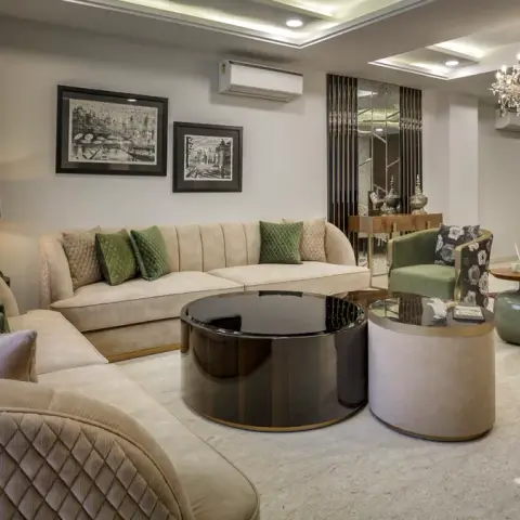 Formal living room where two diamond-quilted cream sofas wrap a black-glass drum table, olive velvet armchairs sit against a reeded mirror screen