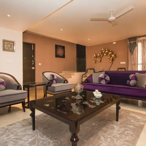 Formal living room with a purple velvet nailhead sofa facing two grey tub chairs, a heavy dark-wood glass-top table on a grey damask rug