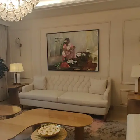 Formal living room with panel-moulded walls, a tufted cream sofa and chaise, organic wood coffee tables, and a large framed figurative painting above the sofa.