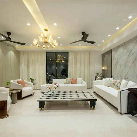 Formal living room with white sofas and pink floral cushions arranged around a black-and-white checkerboard coffee table beneath a gold sputnik chandelier