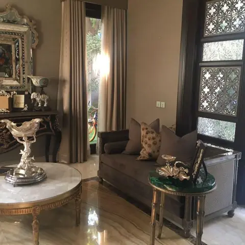 Formal sitting area with a gilt antique console under a Venetian mirror, velvet sofa, and marble coffee table beside an ornate wrought-iron glazed door.