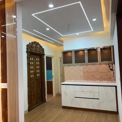 Foyer passage with a floating marble-front crockery unit and diamond-mirror backsplash, cove-lit pop ceiling, and a hand-carved wooden pooja-style door beyond.
