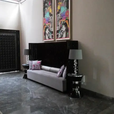 Foyer with a black studded main door, a grey bench sofa backed by a black slatted screen and flanked by two crystal-stem table lamps