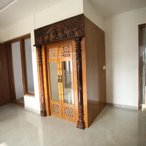 Free-standing pooja room enclosure in the entry foyer with hand-carved traditional wooden doors, pillared surround, and a floral fretwork transom