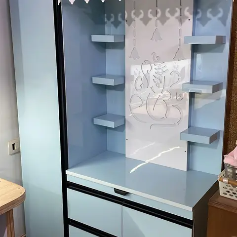 Free-standing pooja unit in glossy pastel-blue laminate with a laser-cut Ganesh motif back panel, corner idol shelves