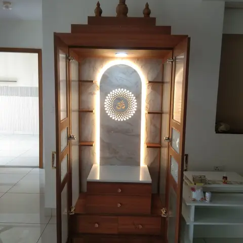 Free-standing pooja unit with a temple-dome pediment, backlit arched Om jaali panel, glass display doors, and drawer storage below.