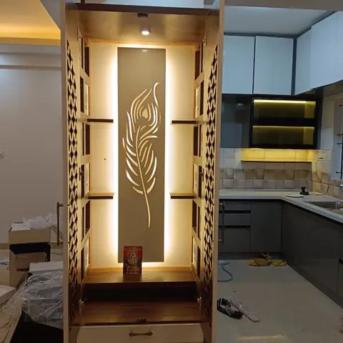 Free-standing pooja unit with jaali-patterned side doors and a backlit wood panel carved with a peacock-feather motif, drawer storage below