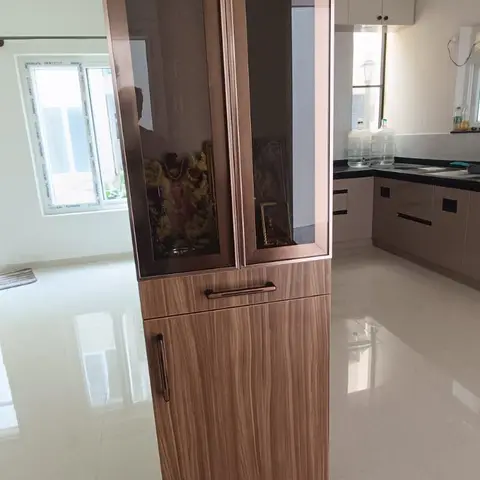 Free-standing pooja unit with tinted mirror-glass upper doors framed in rose-gold trim over a wood-grain laminate base cabinet