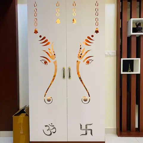 Free-standing white pooja cabinet with a mirrored CNC-cut Ganesha-ear motif and Om and swastik cutouts on the double doors, brass handles.