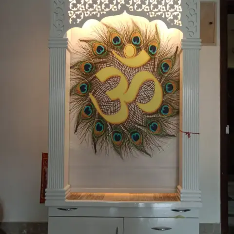 Free-standing white pooja mandir with fluted pillars, a jaali-cut cornice and a backlit peacock-feather Om panel above storage drawers.