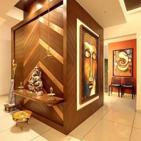 Freestanding chevron-veneer pooja pillar with a brass Ganesha on a floating teak shelf, a hanging brass lamp and spot-lit soffit