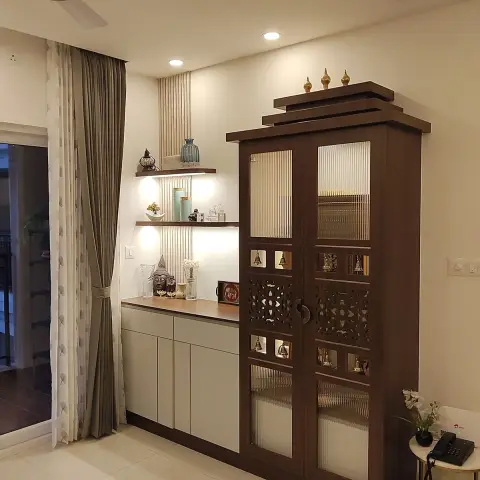 Freestanding dark-wood mandir with reeded-glass shutters, a CNC jaali band, brass bells set into cut-outs and three brass finials on a stepped cornice