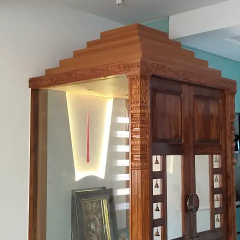 Freestanding glass-walled mandir cabin in a corner of the home, with a stepped teak gopuram cornice