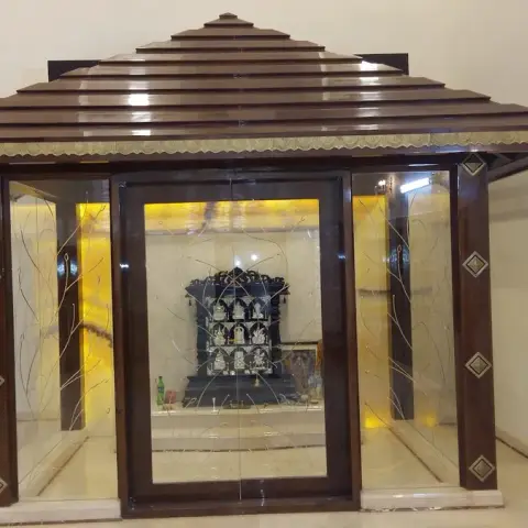Freestanding glass-walled mandir with a stepped teak pagoda roof and a carved brass fascia band