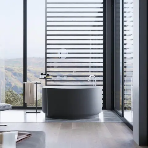 Freestanding matte black oval soaking tub in a glass-walled bath opening onto hill views, with a leather lounge chair and ottoman to the side.