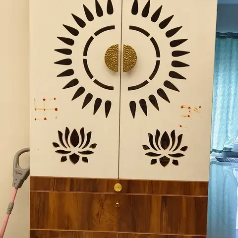 Freestanding pooja cabinet with a sunburst jaali-cut door, lotus motif cutouts, brass bells, and a temple-pediment cornice above a wood-finish base.