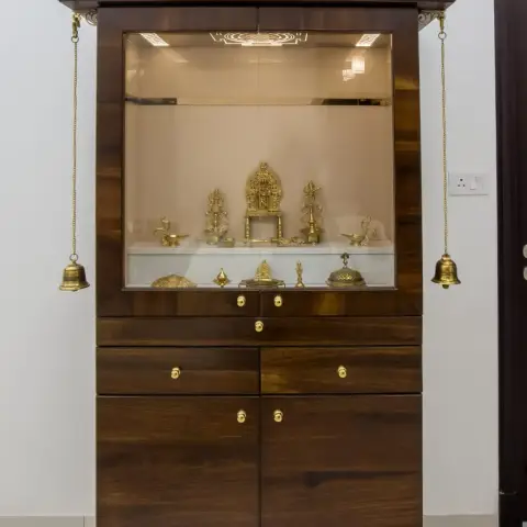 Freestanding teak mandir with a stepped temple pediment topped by eleven brass kalash finials, brass bells hanging on chains from its brackets