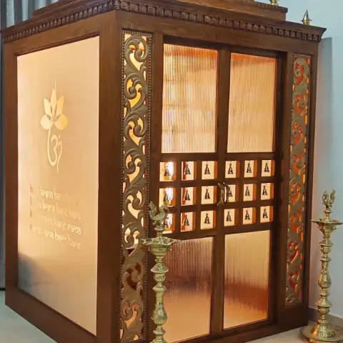 Freestanding walk-in teak mandir with a carved multi-tier gopuram cornice and brass finials, reeded-glass double doors set with a grid of brass deity tiles