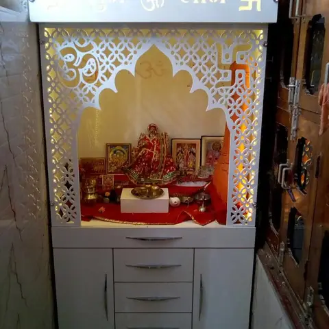 Freestanding white pooja unit with a backlit perforated jaali arch, 'Shubh Labh' signage panel above, and a lower cabinet with drawers and shutters for storage.