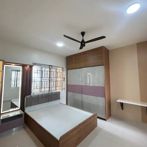 Freshly finished bedroom with a wood-and-mauve sliding wardrobe, an LED-lit mirror dressing unit, and a bare bed frame still wrapped in plastic.