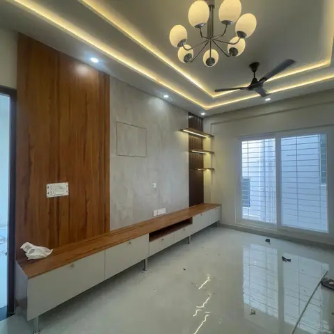 Freshly finished living room with a long wood-and-white TV console, a layered cove-lit false ceiling, and construction debris still on the floor.
