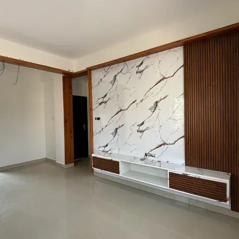 Freshly finished, unfurnished living room with a marble-effect TV feature wall bordered by vertical wood-look fluted panelling and exposed wiring for the TV.