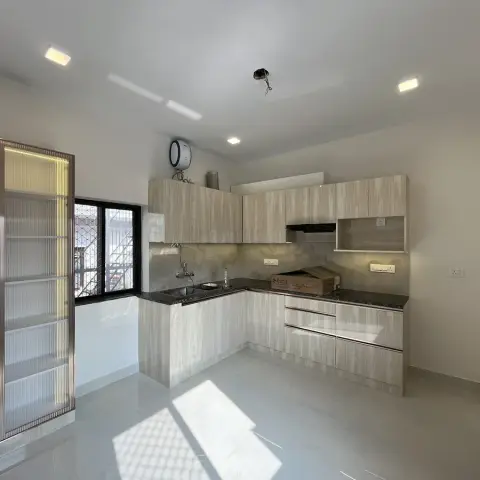 Freshly handed-over L-shaped kitchen with a delivery carton still sitting on the granite counter and a bare wire hanging where the fan hook will go
