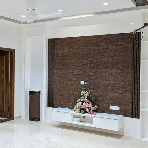 Freshly handed-over living room, still unfurnished, with a wall-hung white TV console and a flower arrangement set against a dark brown textured-stone feature