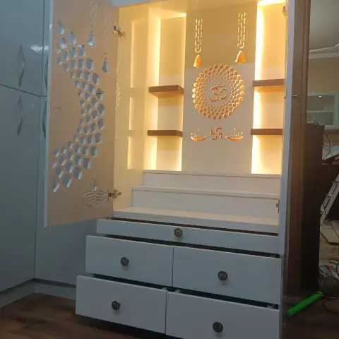 Freshly installed white mandir cabinet with CNC-cut jaali shutters, a backlit Om chakra on the rear panel flanked by warm-lit floating wood shelves